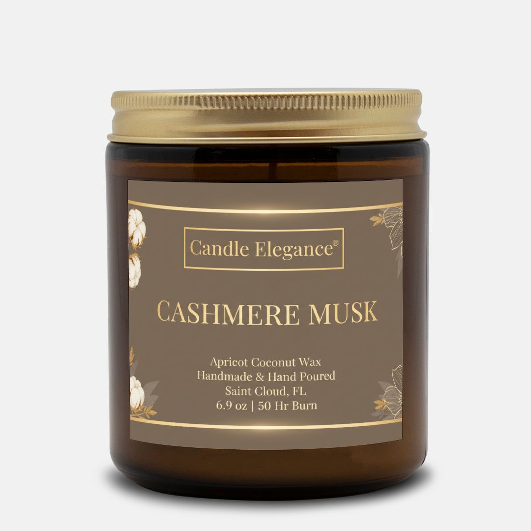 A Candle Elegance Cashmere Musk scented candle in an amber glass jar with a gold metal lid and a brown label, shown on a light gray background.