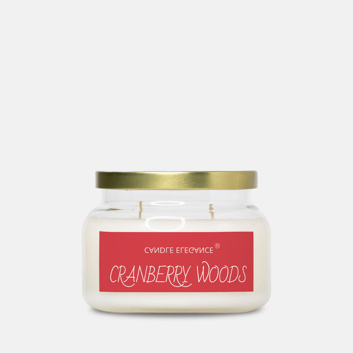 A jar candle with white wax, a gold metal lid, and a red label reading 'CRANBERRY WOODS' on a light gray background.