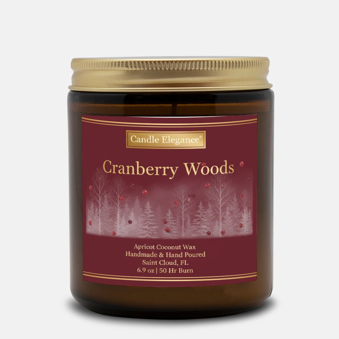 A Candle Elegance 'Cranberry Woods' scented candle in an amber glass jar with a gold metal lid and a dark red label featuring a winter forest design.