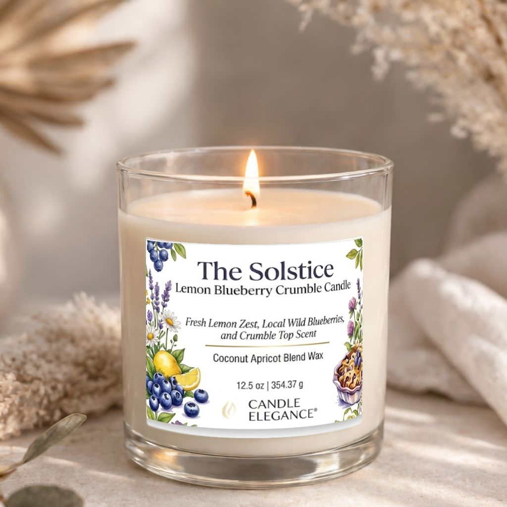 A lit candle in a clear glass jar with a white label reading 'The Solstice Lemon Blueberry Crumble Candle' and 'Candle Elegance' at the bottom. The candle is photographed on a soft neutral surface with dried floral props blurred in the background.