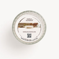 Top-down view of a Candle Elegance Dust Cover 'Spa Day' scented wax candle in a clear textured glass jar, featuring a white paper label with a spa-themed photo and product details.