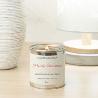 A lit 5 oz candle in a silver metal tin with a cream label reading 'CANDLE ELEGANCE Purely Unscented apricot coconut soy wax blend'. The candle sits on a light wood surface with a textured white vase on the left and a soft-focus lamp in the background.