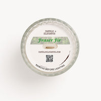 Top-down view of a round dust cover,  textured glass candle with a white wax surface and a printed label reading 'Candle Elegance' and 'Fraser Fir'.