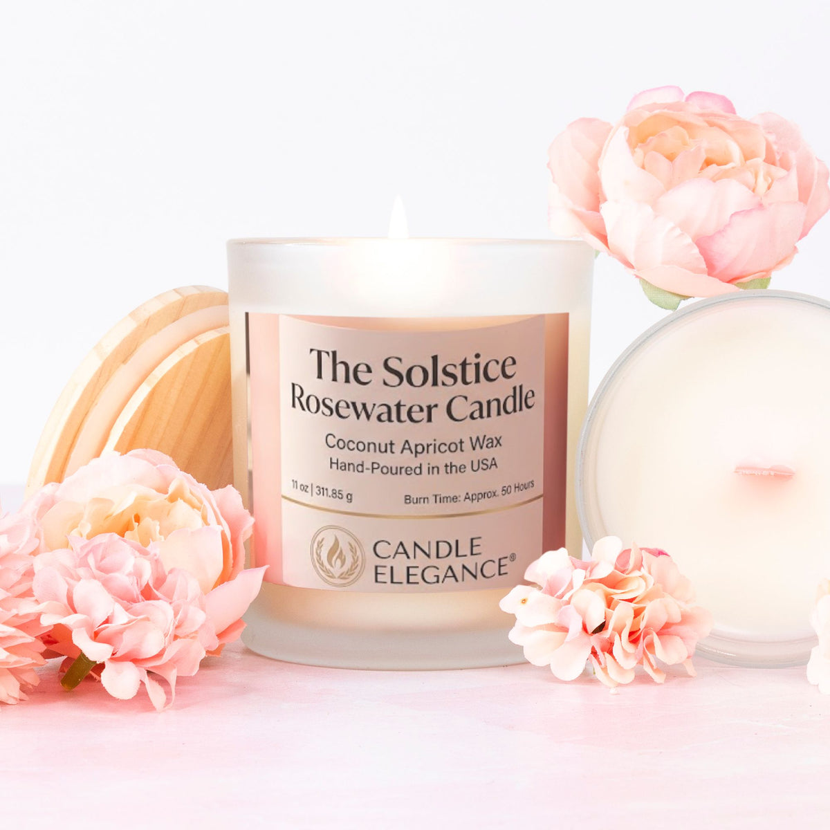 A lit Candle Elegance 'The Solstice Rosewater Candle' in a frosted glass jar, styled with pink flowers and a wooden wick holder on a light pink background.