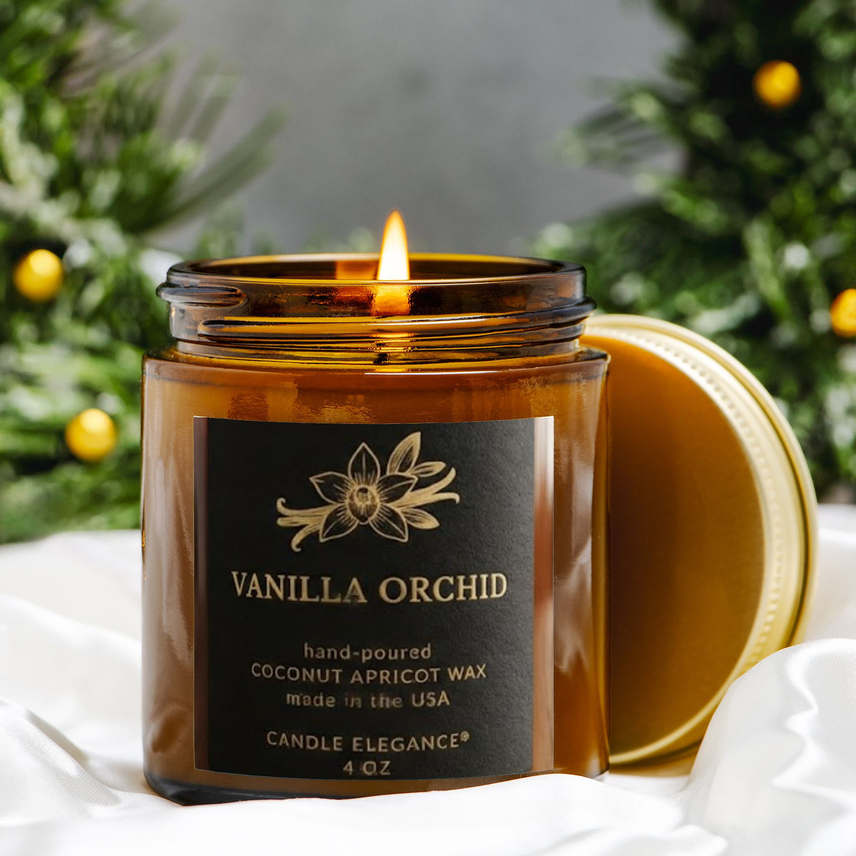 A lit amber glass jar candle labeled Vanilla Orchid by Candle Elegance, with a gold lid resting beside it on white fabric, set against a blurred holiday greenery background.