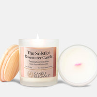 A lit white glass candle jar labeled 'The Solstice Rosewater Candle' by Candle Elegance, shown with a light wood lid on the left and the open wax pool on the right against a light gray background.