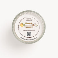 Top-down view of a Candle Elegance dusto cover, 'Mango & Coconut Butter' scented candle in a clear textured glass jar, showing the white wax surface and printed label.