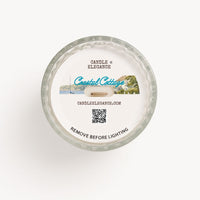 Top-down view of a round glass candle with a white wax surface and printed label reading 'Candle Elegance' and 'Coastal Cottage' on a clean white background.