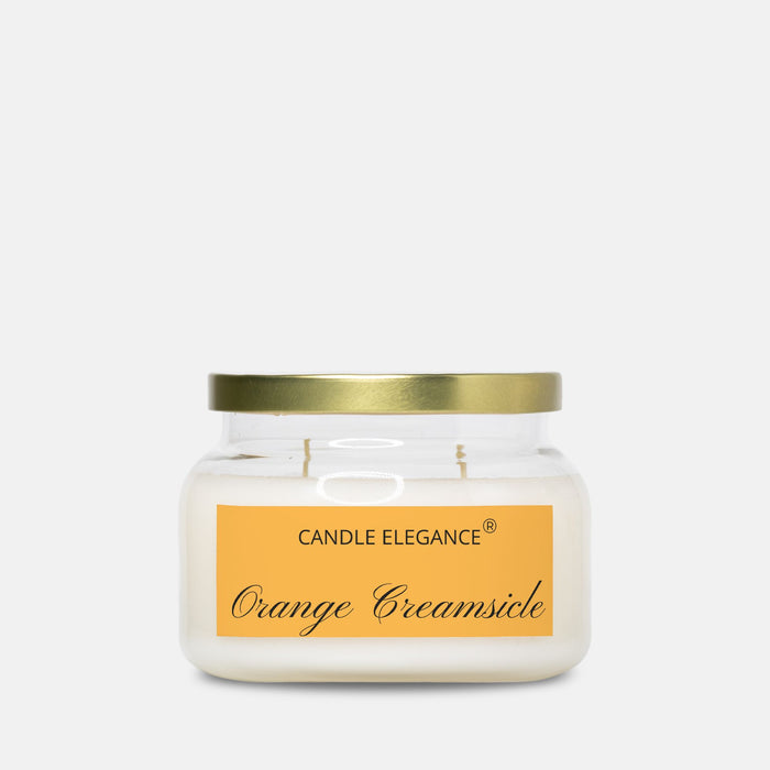 A jar candle with creamy off-white wax, a gold metal lid, and a yellow-orange label reading 'CANDLE ELEGANCE' and 'Orange Creamsicle' on a light gray background.