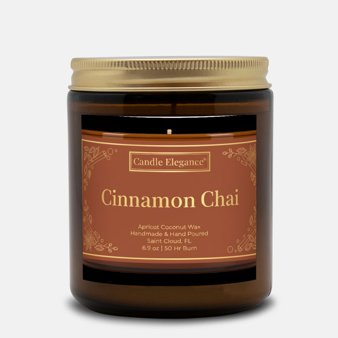 A Candle Elegance Cinnamon Chai scented candle in an amber glass jar with a gold metal lid and a brown label with gold text, set against a light gray background.