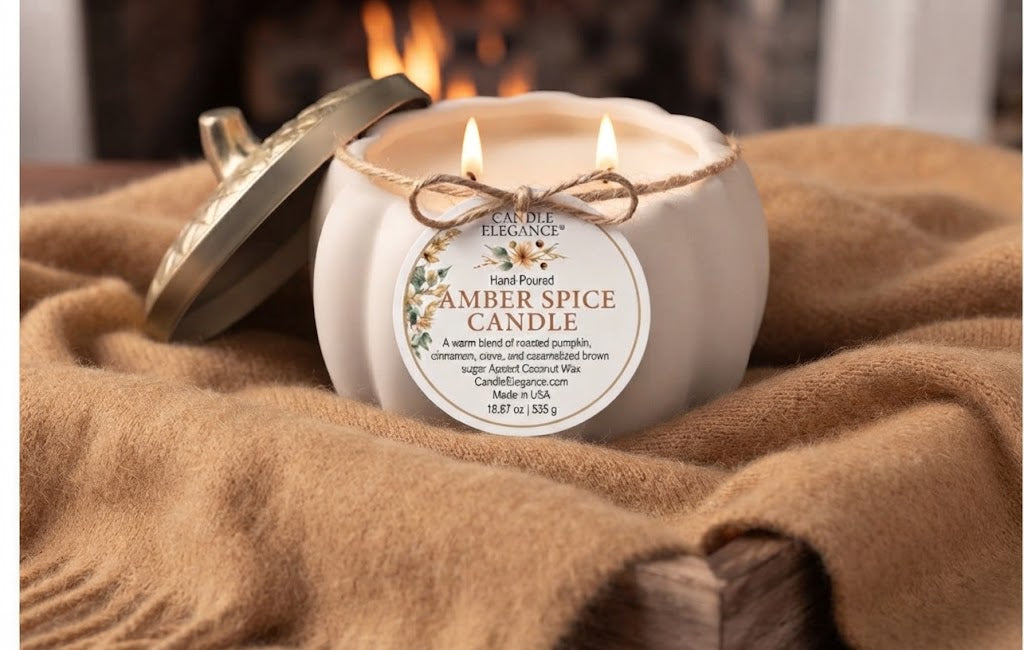 A lit white ceramic candle jar labeled 'Amber Spice Candle' by Candle Elegance, with a metal lid resting beside it on a tan knit blanket in front of a blurred fireplace.