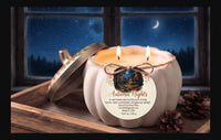 A white pumpkin-shaped candle with a gold-toned lid resting beside it on a wooden tray, lit with two flames. The candle has a round paper label reading 'Autumn Nights' and is styled with pinecones in front of a window showing a night sky and moon.