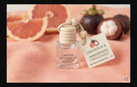 A Grapefruit & Mangosteen candle diffuser refill by Candle Elegance, featuring a clear glass bottle with a light wood cap and a hanging paper tag, styled on a peach fabric background with grapefruit and mangosteen slices.