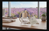 A glass fragrance diffuser bottle with a wooden bead top and a small card reading 'Lavender Candle Experience' sits on a wooden table in front of a large window overlooking a lavender field.