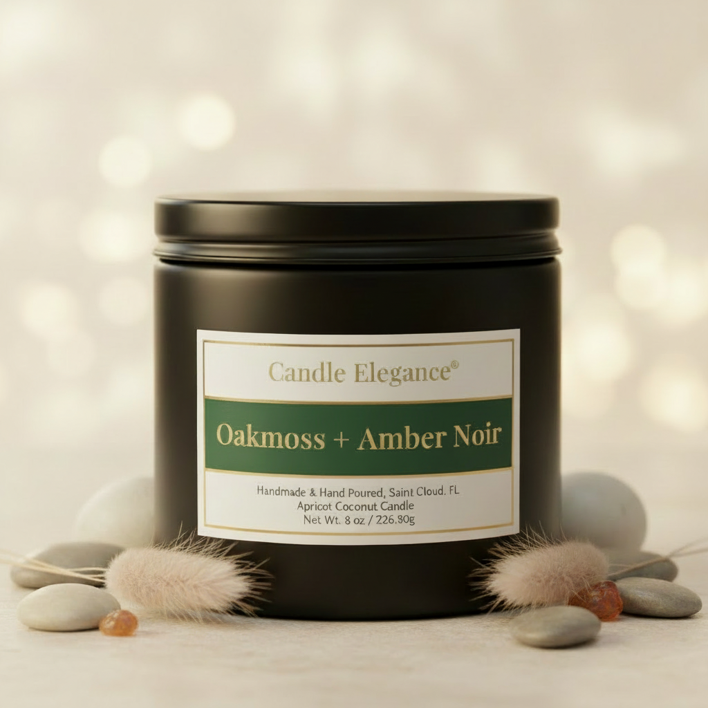 A matte black metal candle tin with a cream and green label reading 'Candle Elegance Oakmoss + Amber Noir,' styled with faux fur and smooth stones on a warm beige surface against a softly blurred bokeh background.