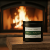 A black candle tin labeled 'Candle Elegance Oakmoss + Amber Noir' sits on a wooden mantel in front of a warm, glowing fireplace.