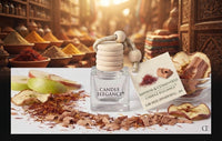 A glass candle diffuser bottle labeled 'CANDLE ELEGANCE' with a stacked wooden wick holder and a product tag reading 'SABRON & CEDARWOOD CANDLE ELEGANCE CUBE MOOD DIFFUSER REFILL - 240'. The bottle is styled on a white surface with cinnamon, apple slices, and spices in a warm, rustic apothecary-style setting.