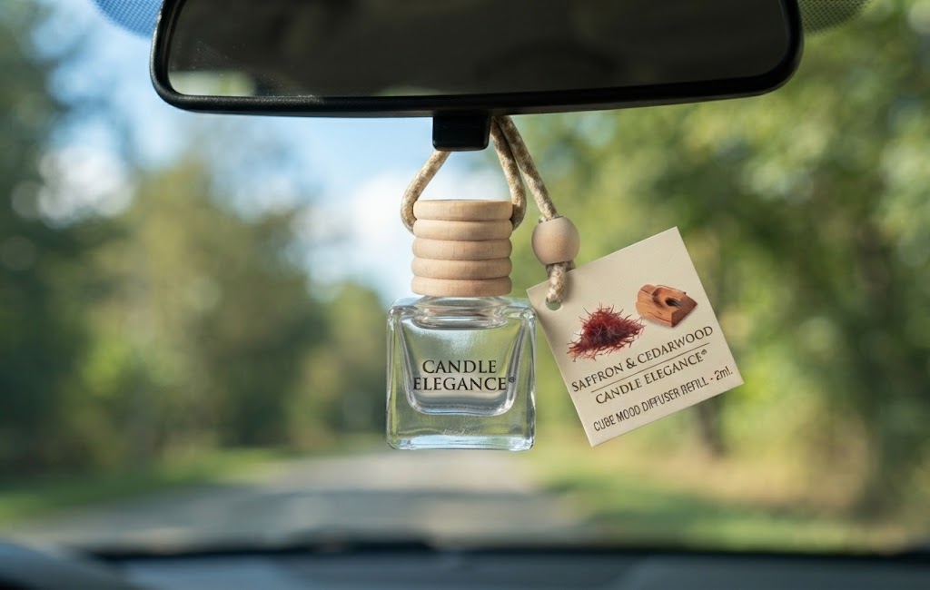 A Carvewood & Cedarwood Saffron & Rose fragrance diffuser bottle hanging from a car's rearview mirror, with a paper tag attached showing the scent details.