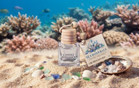 A Sea Minerals Candle Elegance cube wood diffuser bottle with a wooden lid and decorative tag, styled on a sandy beach with seashells and a shell dish against an underwater coral background.