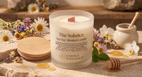A frosted glass jar candle labeled 'The Solstice Spa Day Mindset Candle' by Candle Elegance, styled on a stone surface with daisies, a wooden honey pot, a honey dipper, and gold coins.