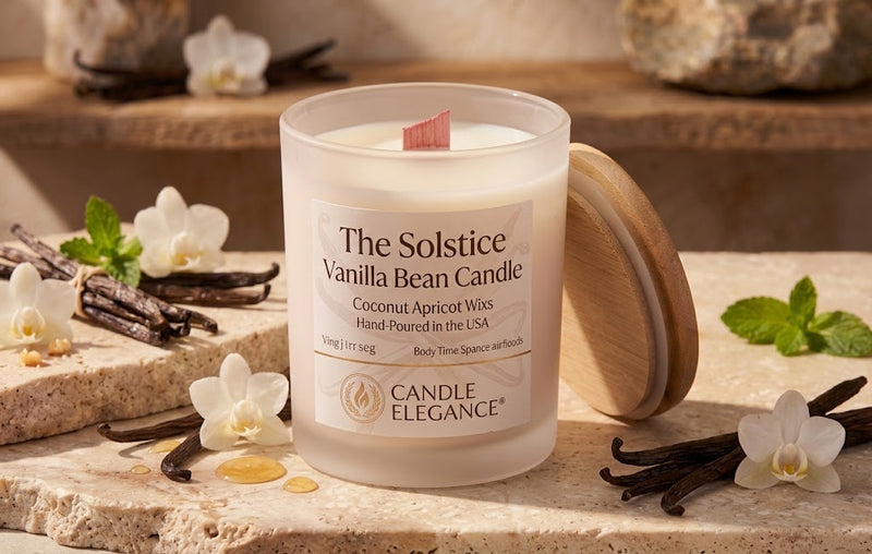 A frosted glass candle jar labeled 'The Solstice Vanilla Bean Candle' by Candle Elegance, shown with a  pink wooden wick & wooden lid leaning against it on a stone surface. Vanilla beans, white flowers, mint leaves, and warm ambient lighting create a styled product scene.