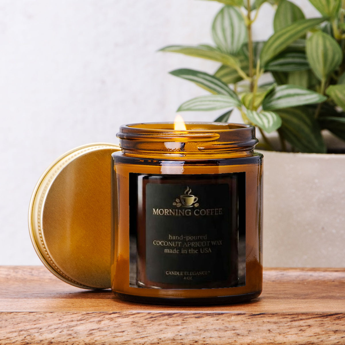 An amber glass jar candle with its lid leaning beside it on a wooden surface. The candle label reads 'MORNING COFFEE' and shows coconut apricot wax.