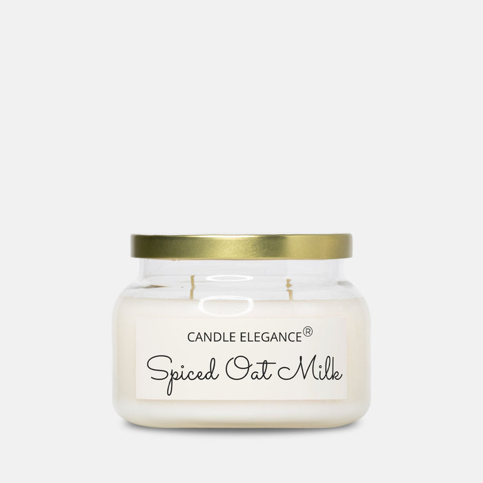 A Candle Elegance 'Spiced Oat Milk' scented candle in a clear glass jar with a gold metal lid and a white label, set against a solid light gray background.