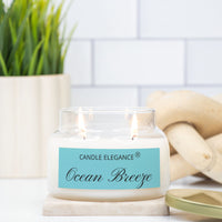 A jar candle with white wax, a gold metal lid, and a light blue label reading 'CANDLE ELEGANCE' and 'Ocean Breeze' on a light gray background.