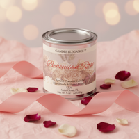 A tin candle labeled 'Candle Elegance Bohemian Rose' sits on pink fabric with scattered rose petals and ribbon. The candle tin has a silver lid and a cream label with pink script and floral artwork.