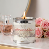 A lit CANDLE ELEGANCE 'Bohemian Rose' apricot coconut candle in a silver tin container, styled on a white marble surface with pink roses and a perfume bottle in the background.