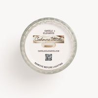 Top-down view of a Candle by Elegance 'Cashmere Vanilla' scented candle in a clear glass jar, showing the white wax surface and printed label details.
