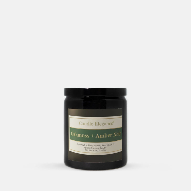 A black glass jar candle with a black lid and a cream label reading 'Candle Elegance' and 'Oakmoss + Amber Noir', photographed on a clean white background.