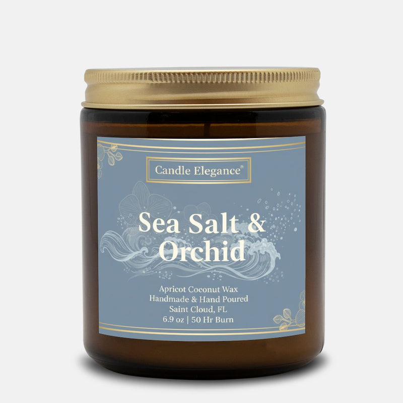 A Candle Elegance 'Sea Salt & Orchid' scented candle in an amber glass jar with a gold metal lid and a dusty blue label, set against a light gray background.