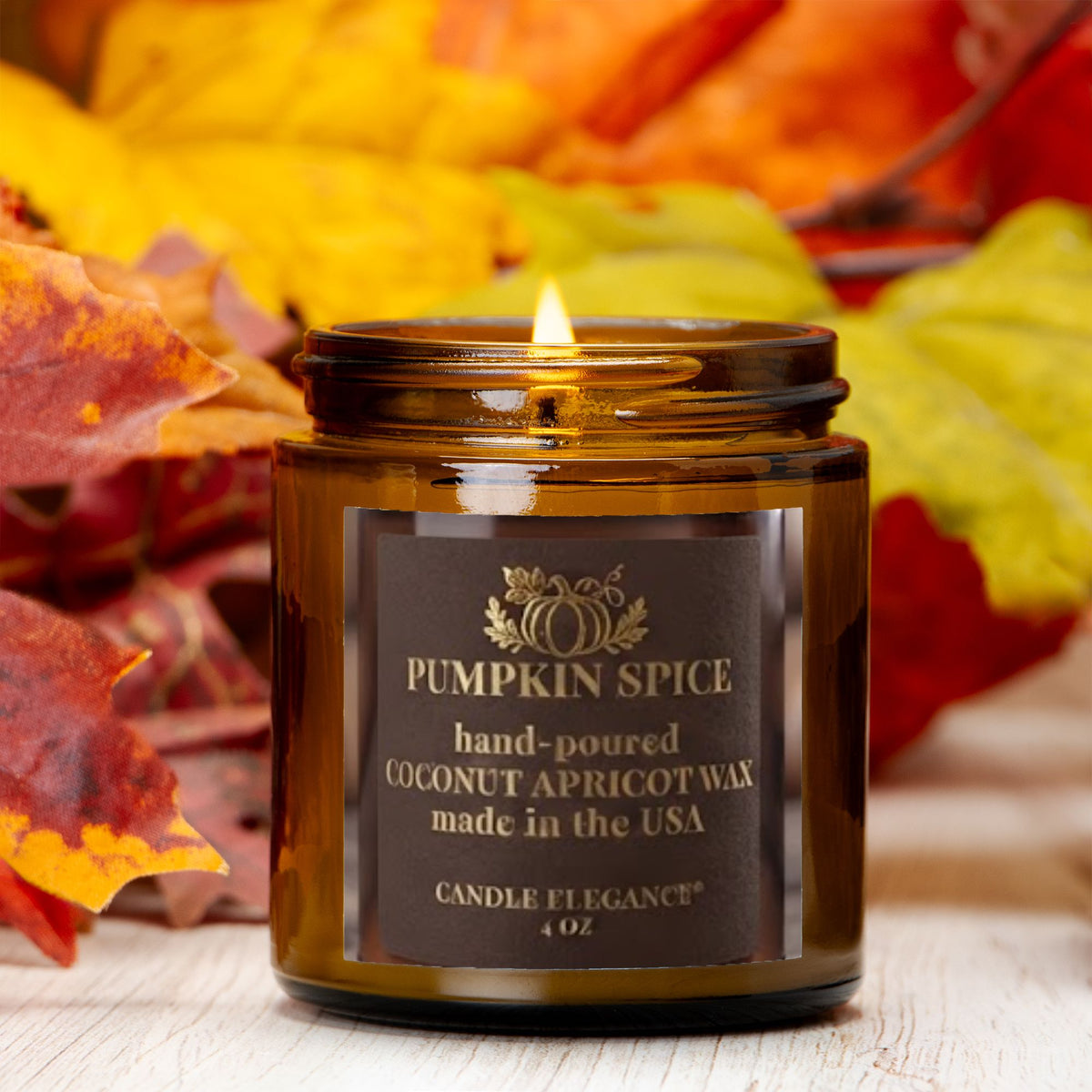 A lit amber glass jar candle labeled 'Pumpkin Spice' by Candle by Elegance, set against a background of colorful autumn leaves on a light wood surface.