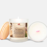 A frosted glass jar candle labeled 'The Solstice Spa Day Mindset Candle' by Candle Elegance, shown with a light wood lid on the left and the open wax pool on the right against a light gray background.