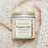 A 4 oz glass jar candle with a white label reading 'Pumpkin Spice' by Candle Elegance, set on a cream-colored textured knit blanket.