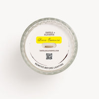 Top-down view of a Candle Elegance 'Bare Essence' candle in a clear glass jar, showing the dust cover over the white wax, textured glass rim, and a yellow label on a white background.
