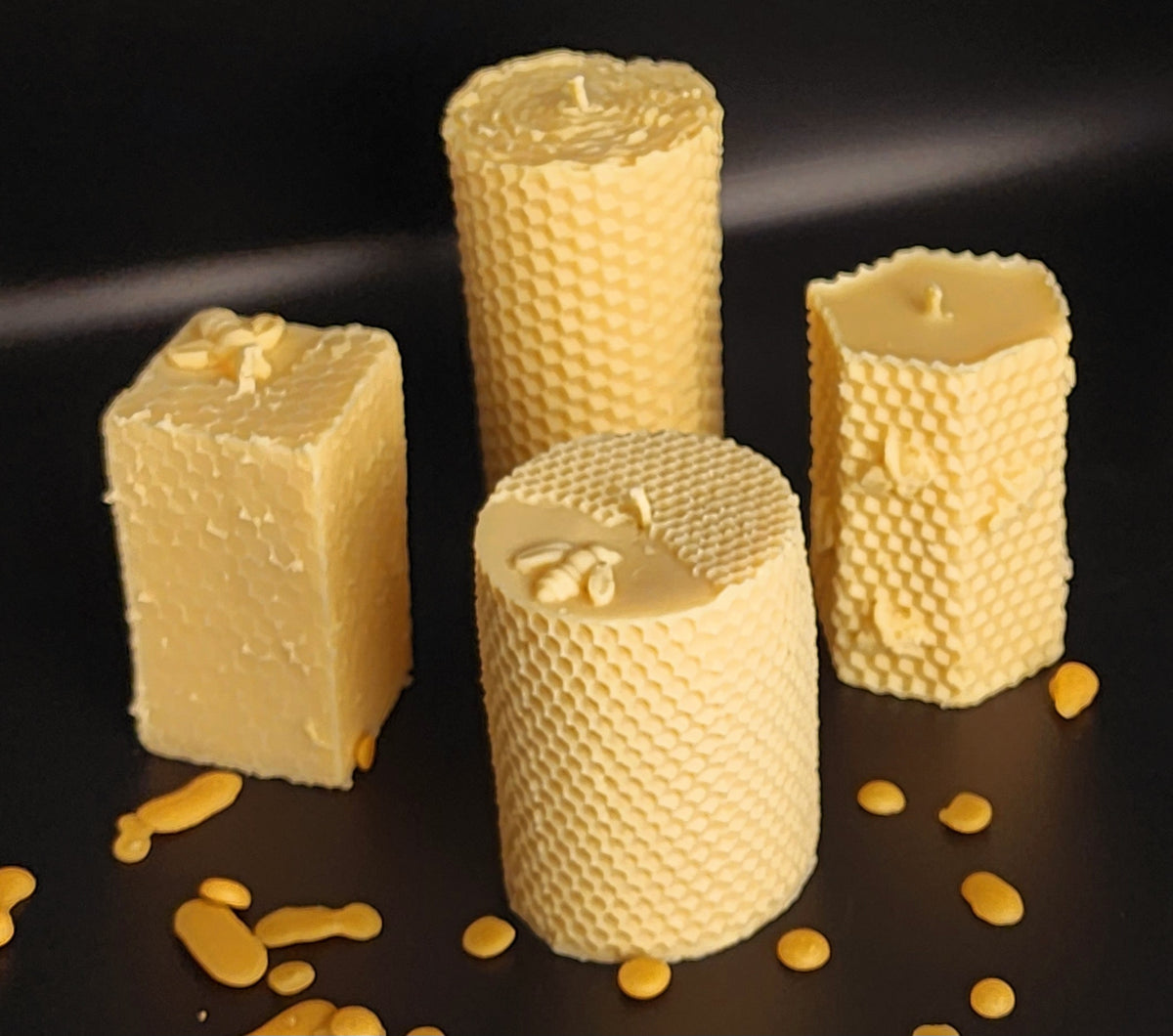 Four textured Organic Pillar beeswax candles on a dark surface with scattered wax pieces.