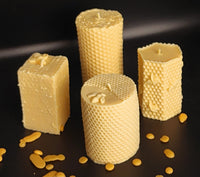 Four textured Organic Pillar beeswax candles on a dark surface with scattered wax pieces.