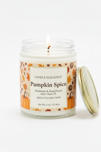 A lit Candle Elegance Pumpkin Spice jar candle with a white wax body, clear glass jar, and a gold metal lid resting beside it on a clean white background.