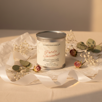 A jar candle labeled 'Candle Elegance Purely Unscented' sits on white tissue paper with dried flowers and greenery around it on a warm beige surface.