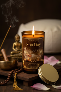 A lit 'Spa Day' candle in a dark amber glass jar sits on a wooden tray with its gold lid beside it. The scene is styled with pink petals, a brass bowl, a incense stick, and a small Buddha statue against a dark, atmospheric background.