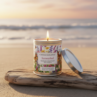 A lit candle in a round metal tin sits on a piece of driftwood at the beach, with the lid leaning beside it. The background shows a softly blurred ocean shoreline at sunset.