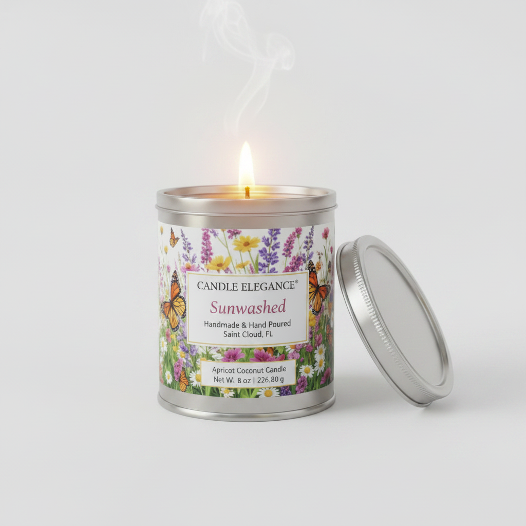 A lit metal tin candle with a floral label reading 'Candle Elegance Sunwashed' and a silver lid resting beside it on a clean light gray background.